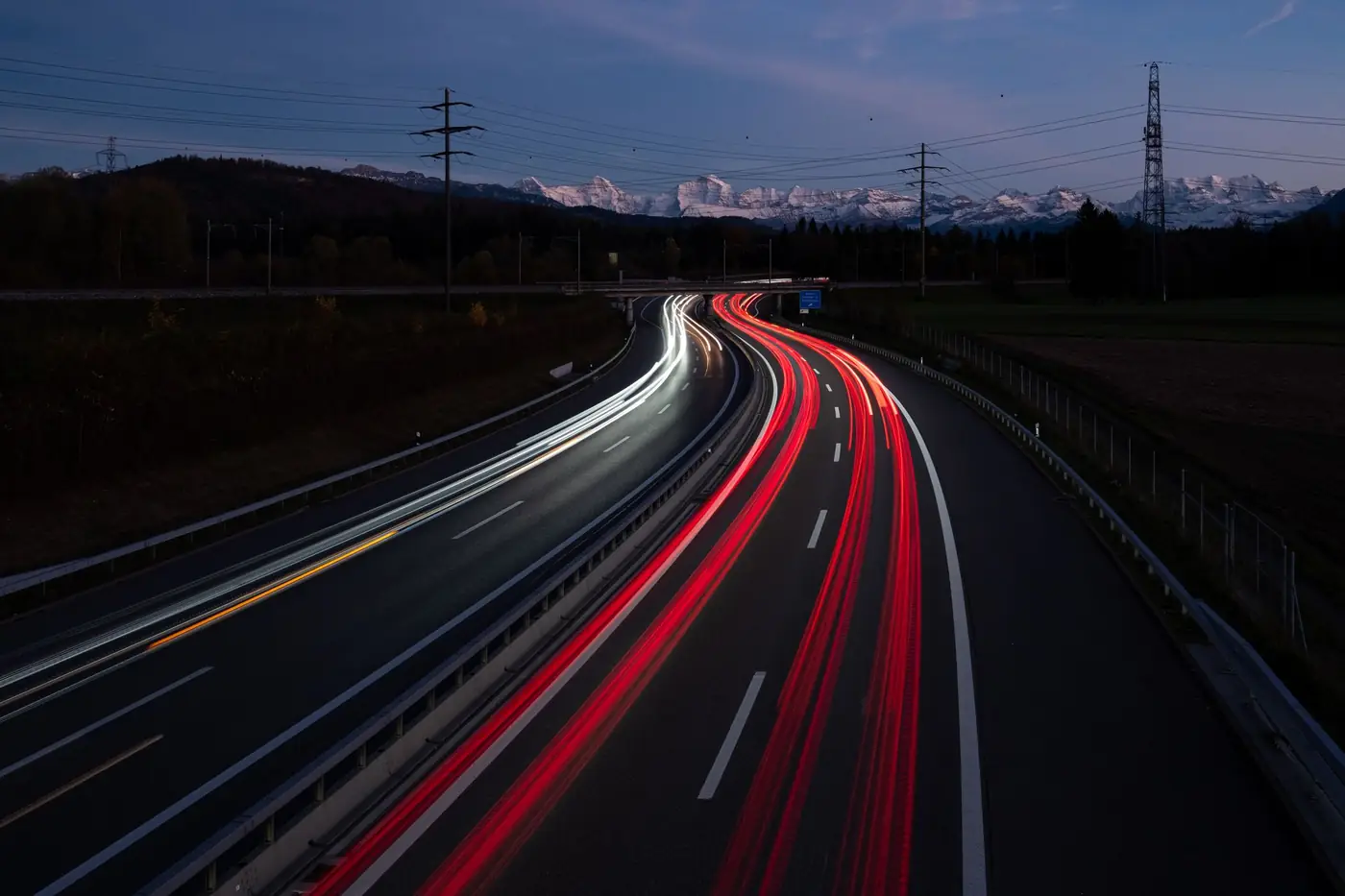Snelweg in de avond met lichtsporen van auto's en bergen op de achtergrond