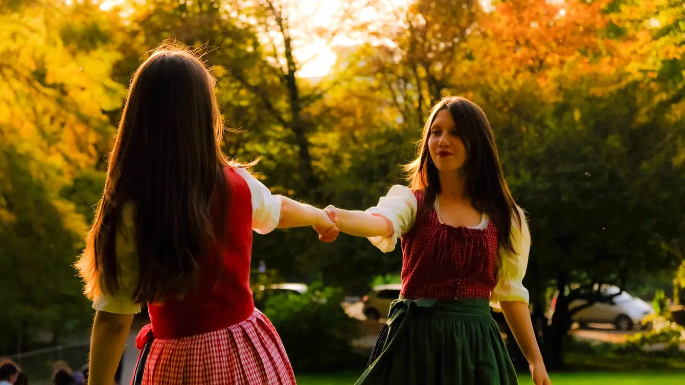 Twee vrouwen in traditionele Oostenrijkse kleding dansen tussen herfstbladeren in een park