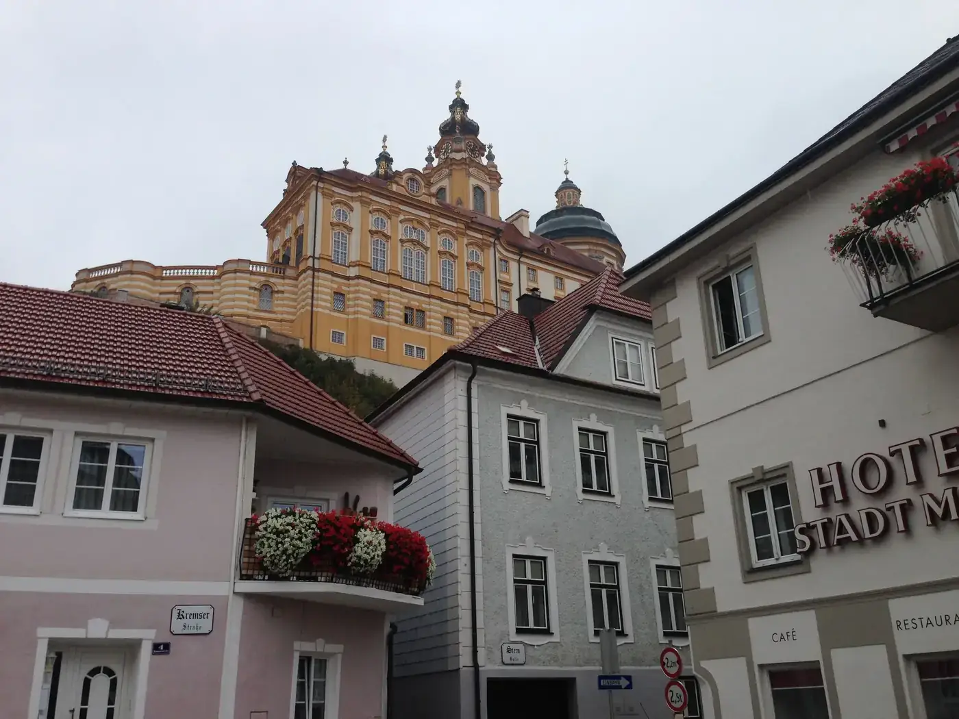 Melk Abbey towers over a quaint street in Melk, Austria, showcasing Baroque architecture on a cloudy day.