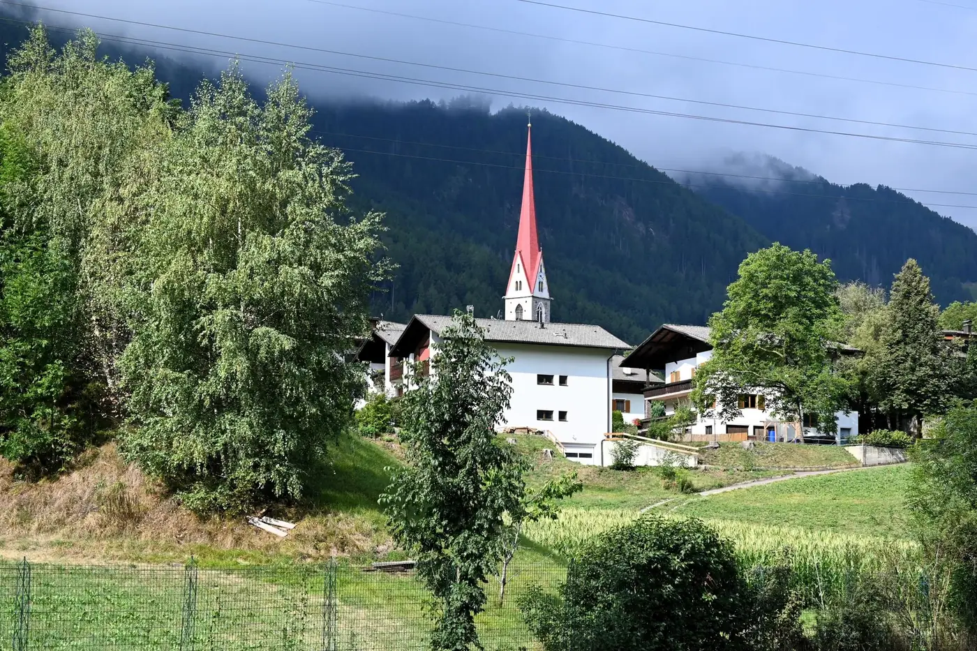 Picturesque church with red steeple among lush mountains in Deutschlandsberg, Austria.