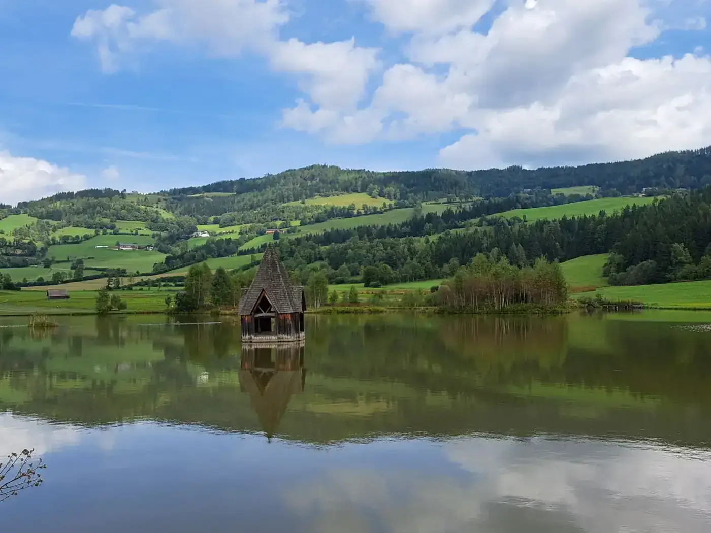 Scenic view of a wooden house on a lake with lush hills in Steiermark, Austria.