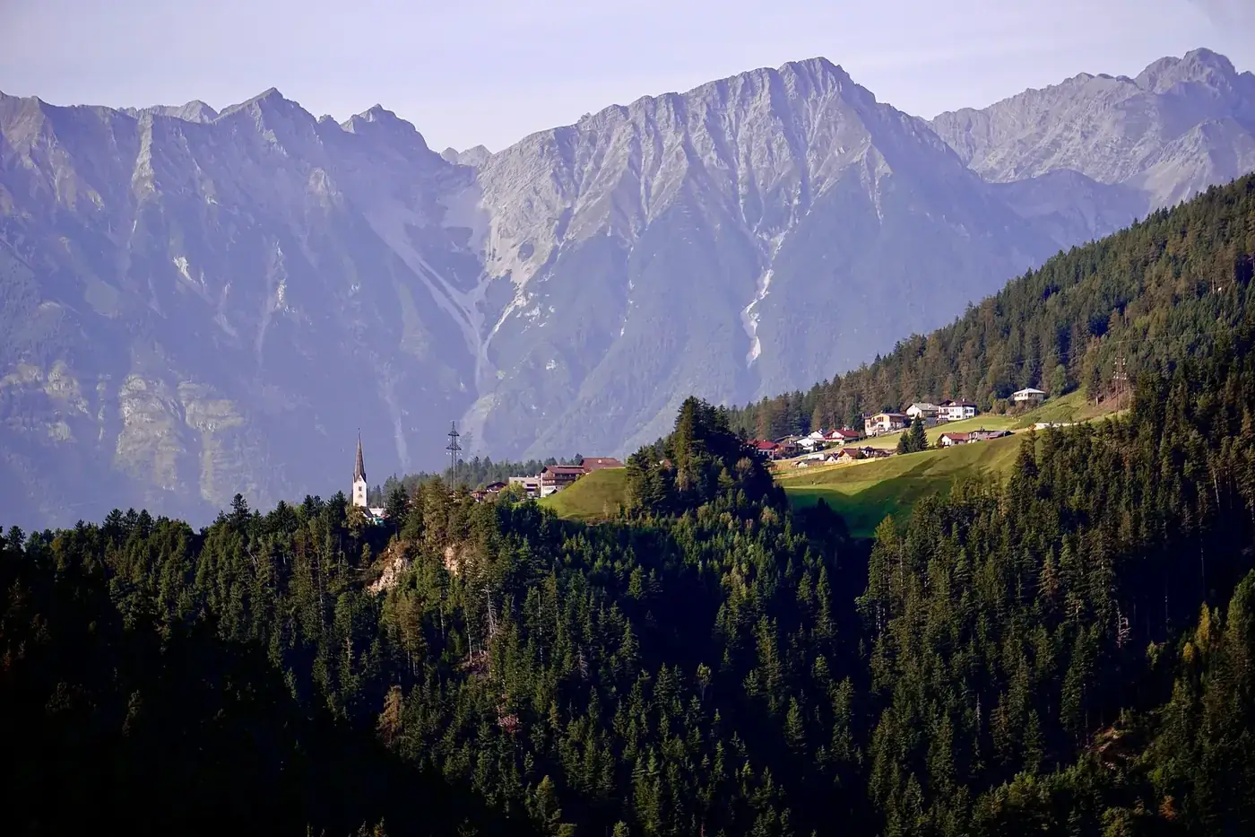Aerial view of a village nestled in the Tyrolean Alps of Austria, surrounded by lush forests and mountains.