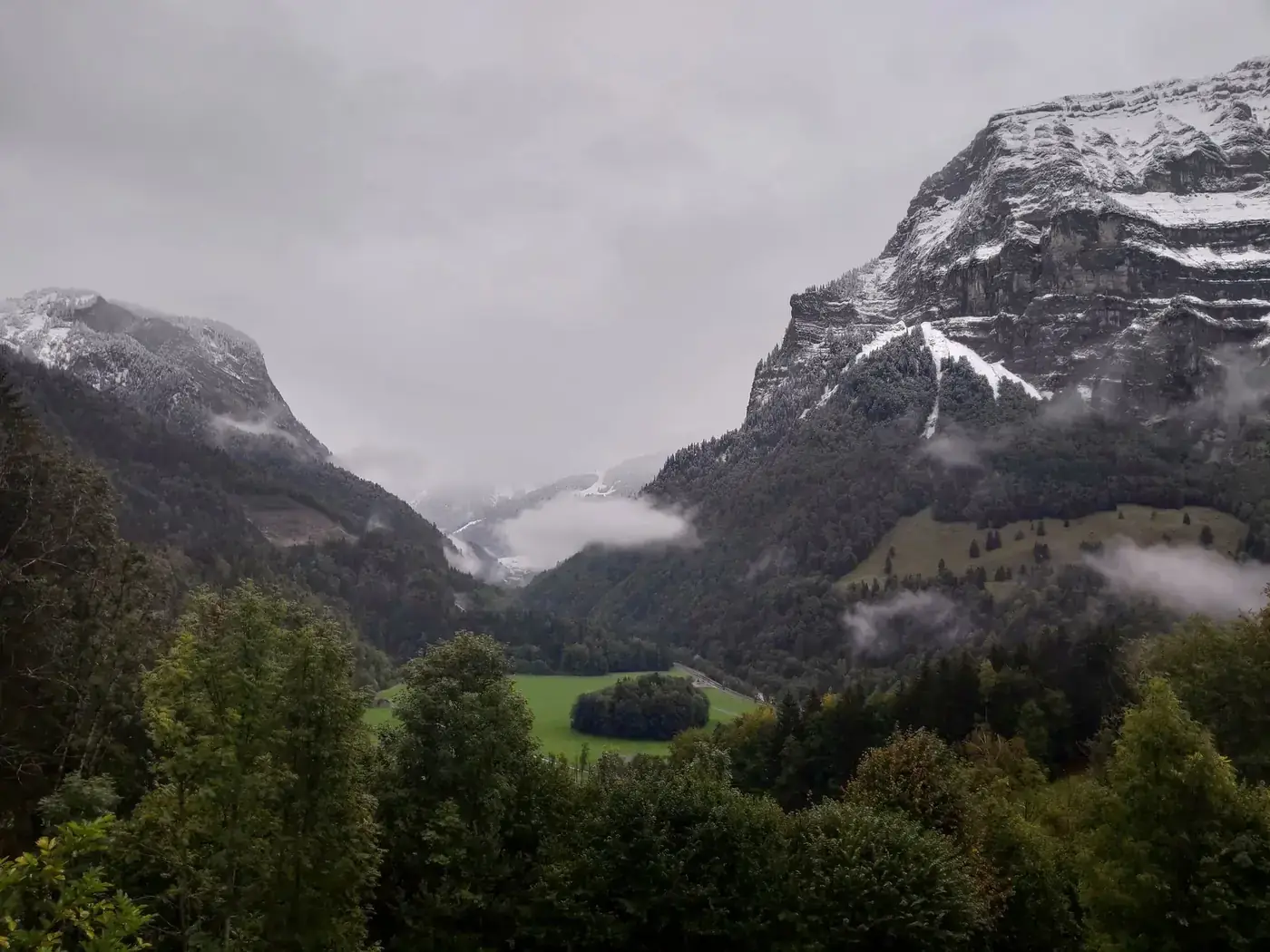 Serene view of misty Schnepfau valley with mountains and greenery, creating a tranquil Alpine atmosphere.