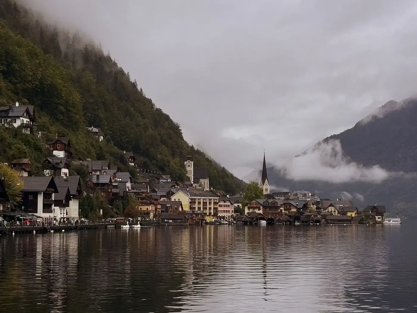 Picturesque village by the lake with misty mountains and charming architecture on a cloudy day.