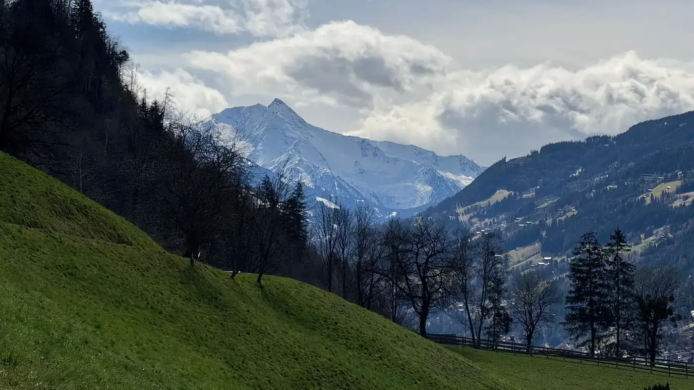 A picturesque view of snowy mountains and lush green hills in the Austrian Alps.