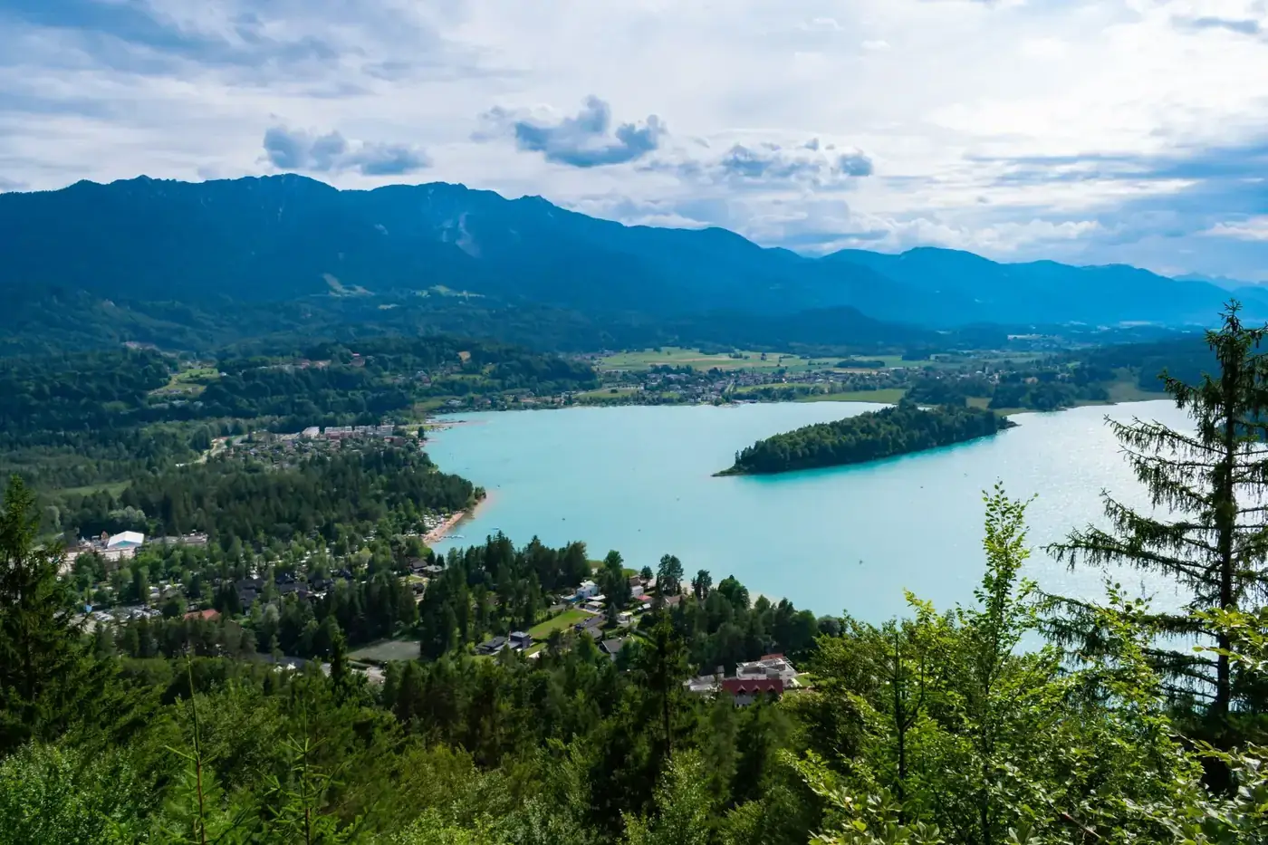 A breathtaking aerial view of Lake Faak surrounded by lush forests and mountains in Austria.