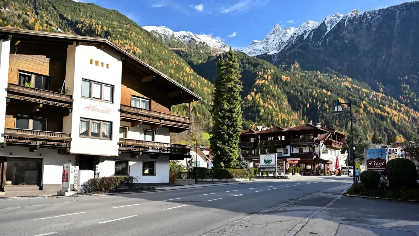 Scenic view of a quaint alpine village in Tyrol, Austria with autumn foliage and snow-capped peaks.