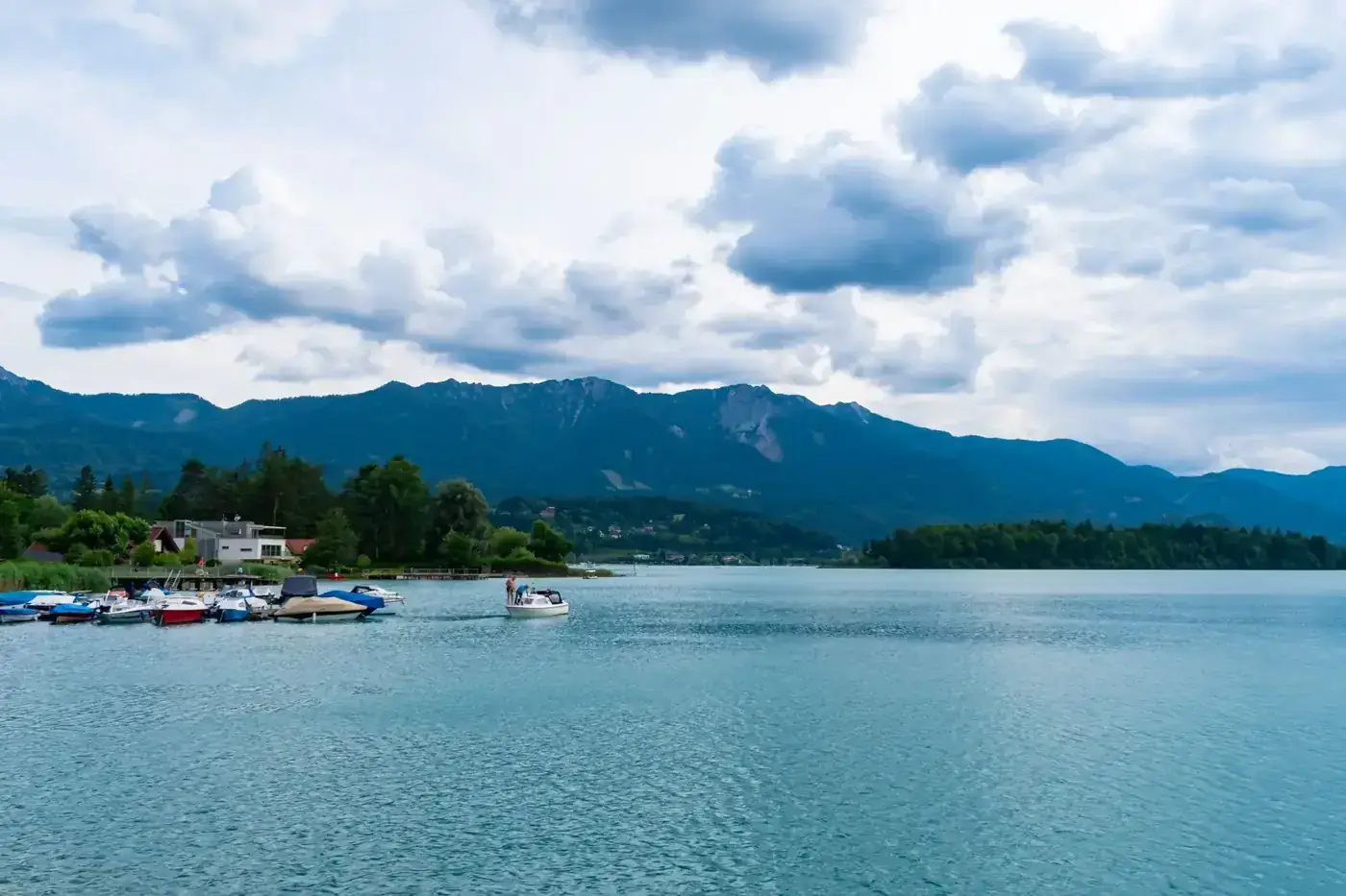 Picturesque lake in Villach, Austria, with boats and mountains under a cloud-filled sky.