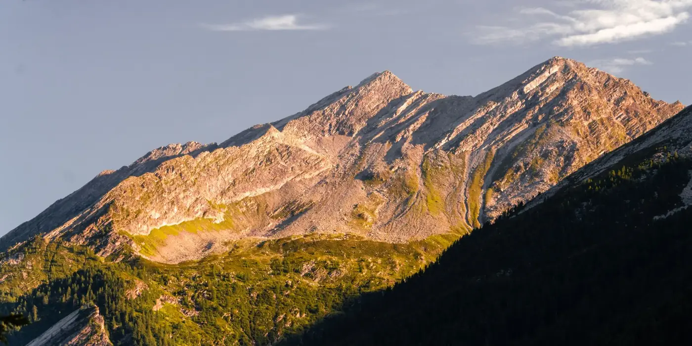 Breathtaking view of a sunlit mountain peak with lush greenery at sunset.