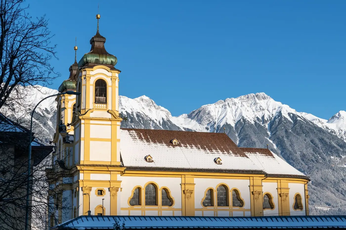 Witlen Basilica against the backdrop of snowcapped Alps in Innsbruck, Austria, under a bright blue sky.