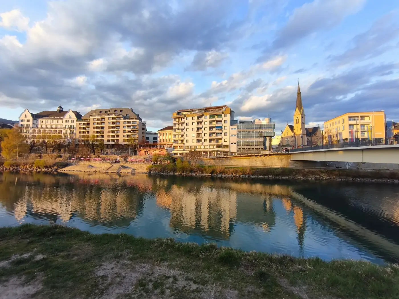 Charming urban landscape in Villach, Austria with riverside reflections and dramatic skies.