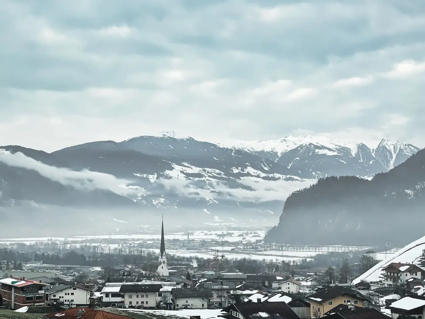 Scenic winter panorama of Jenbach, Tyrol, Austria featuring snow-covered mountains and a picturesque church.
