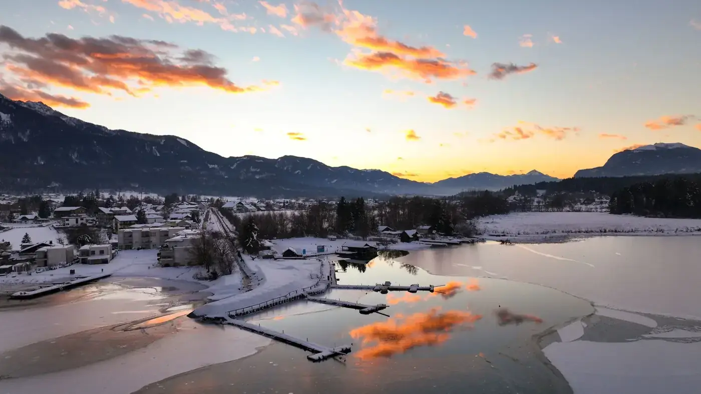 A breathtaking aerial view of a frozen lake in Kärnten, Austria during a winter sunrise.