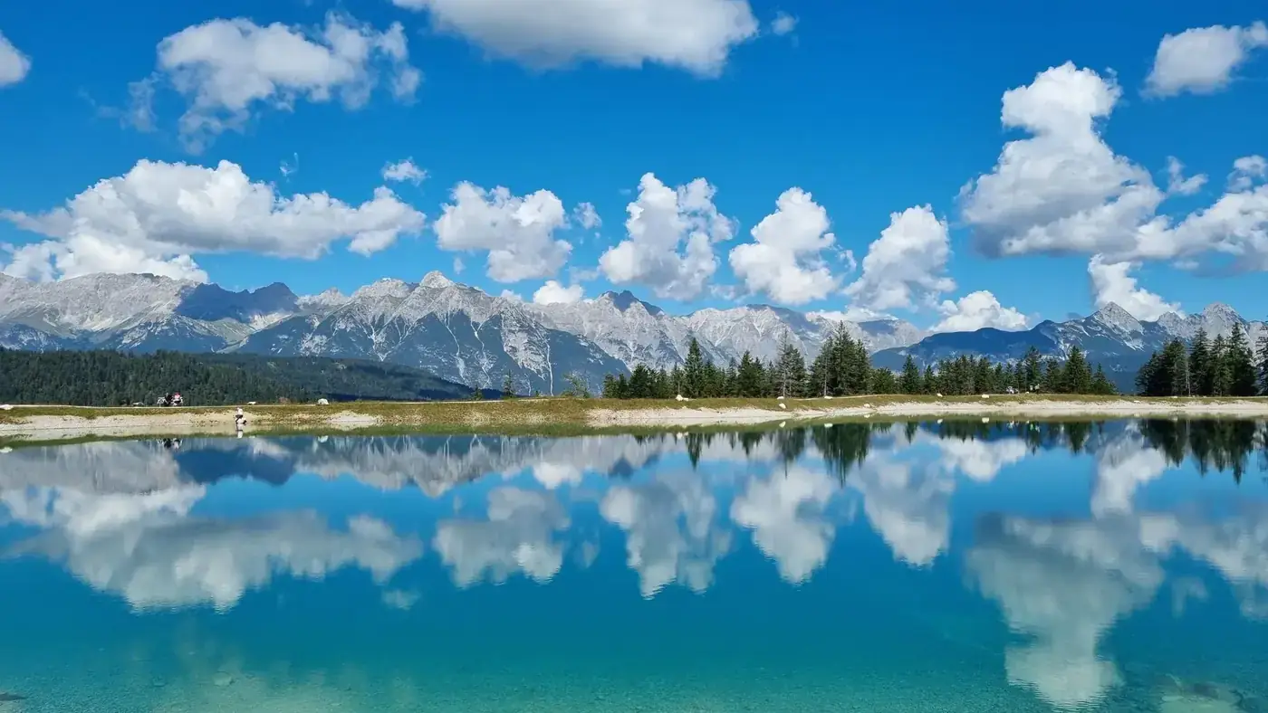 Scenic view of an alpine lake reflecting mountains and clouds in Seefeld, Tyrol, Austria.