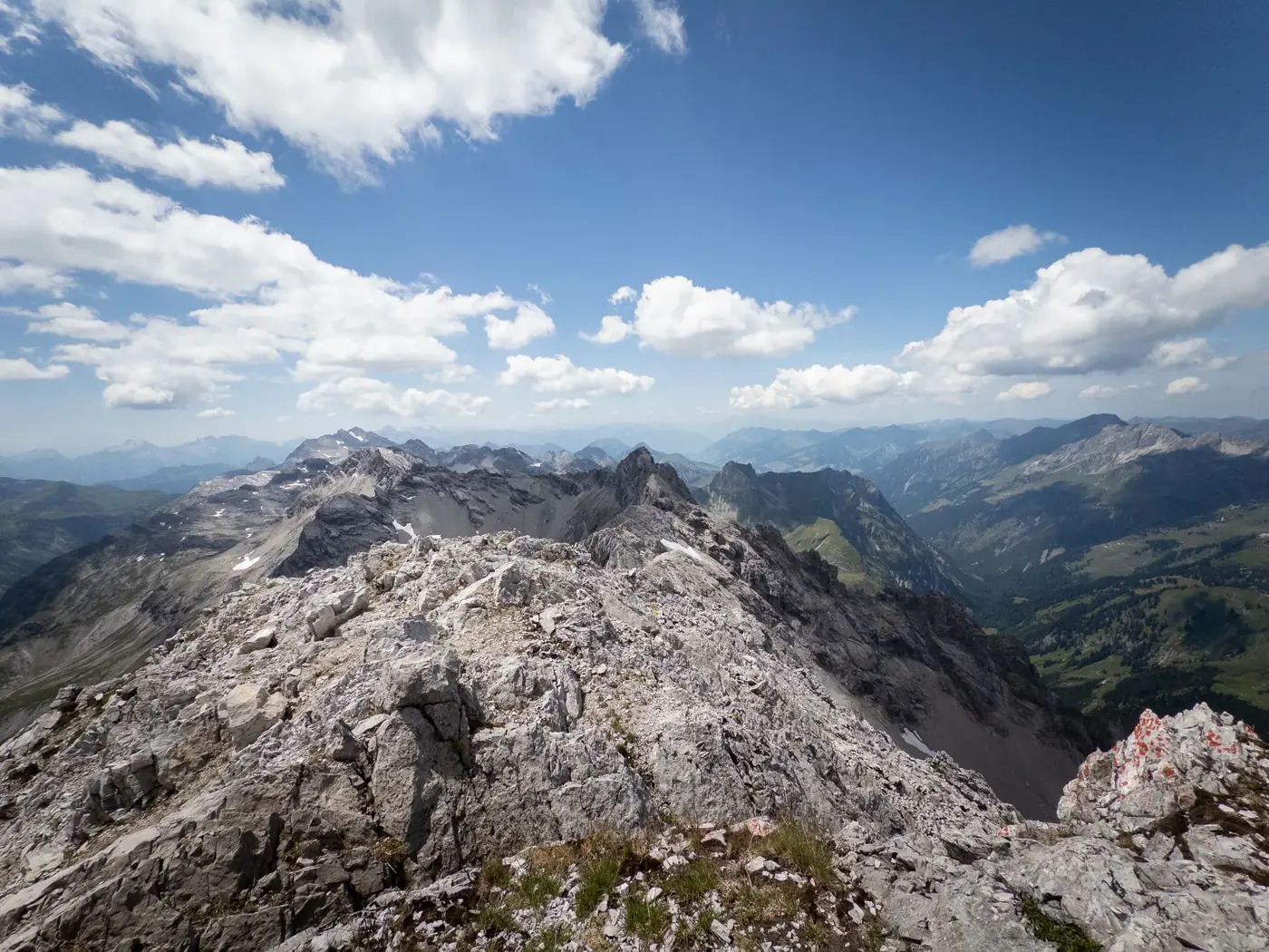 Expansive view of the dramatic Alpine peaks under a bright summer sky with scattered clouds.
