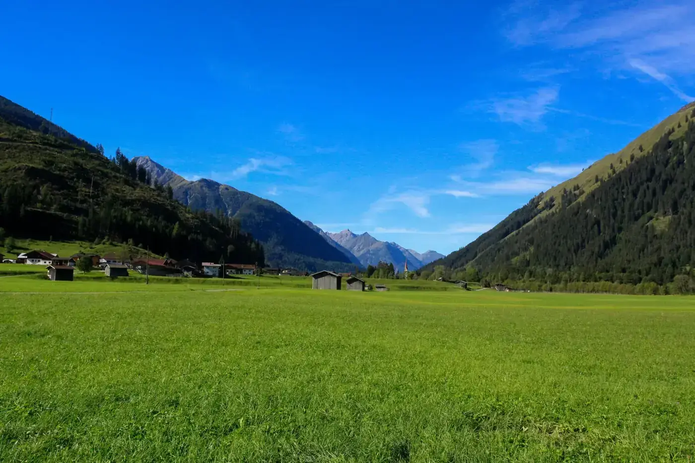 Vibrant summer view of Lech, Austria with lush valleys and distant mountains.