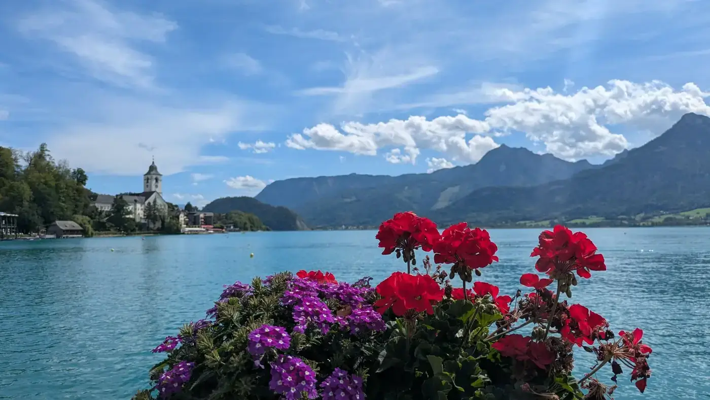 Colorful flowers by the lake with mountain and church view in the background.