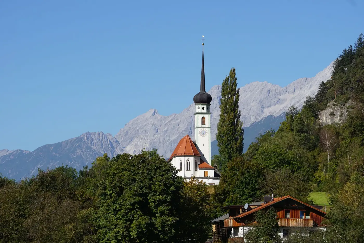 Picturesque view of a historic church surrounded by the Alps and lush greenery in Austria.