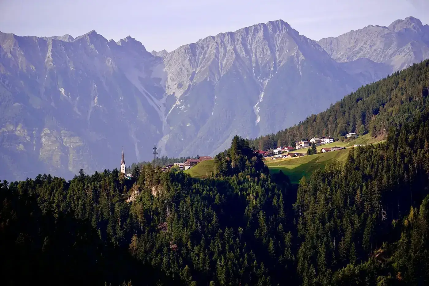 Aerial view of a village nestled in the Tyrolean Alps of Austria, surrounded by lush forests and mountains.