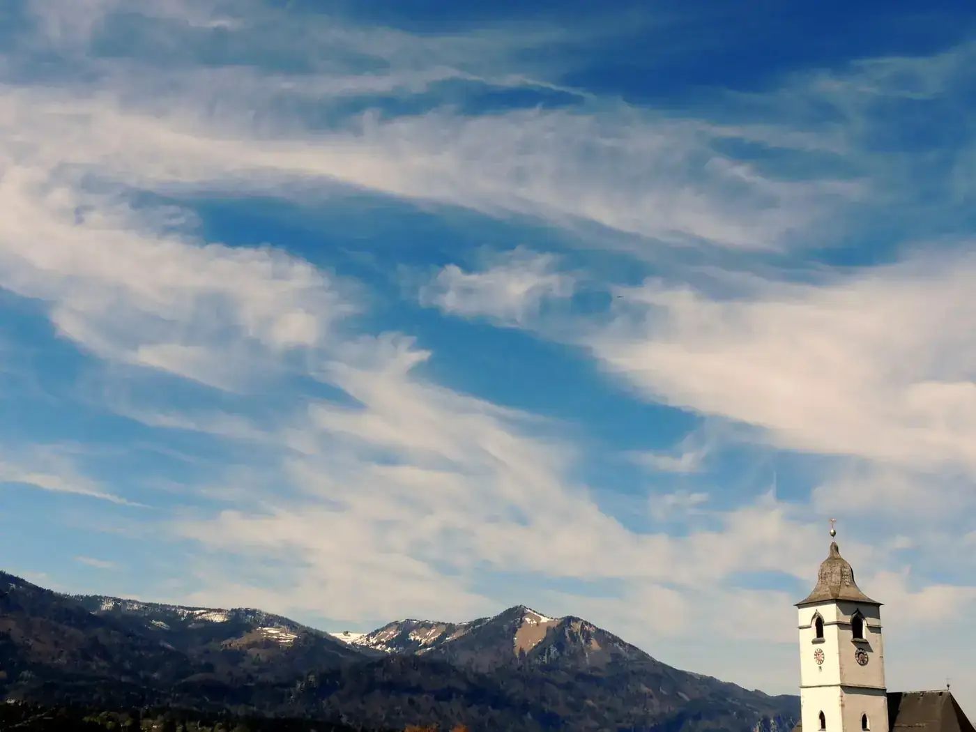 Church tower against Salzkammergut mountains with a vivid blue sky.