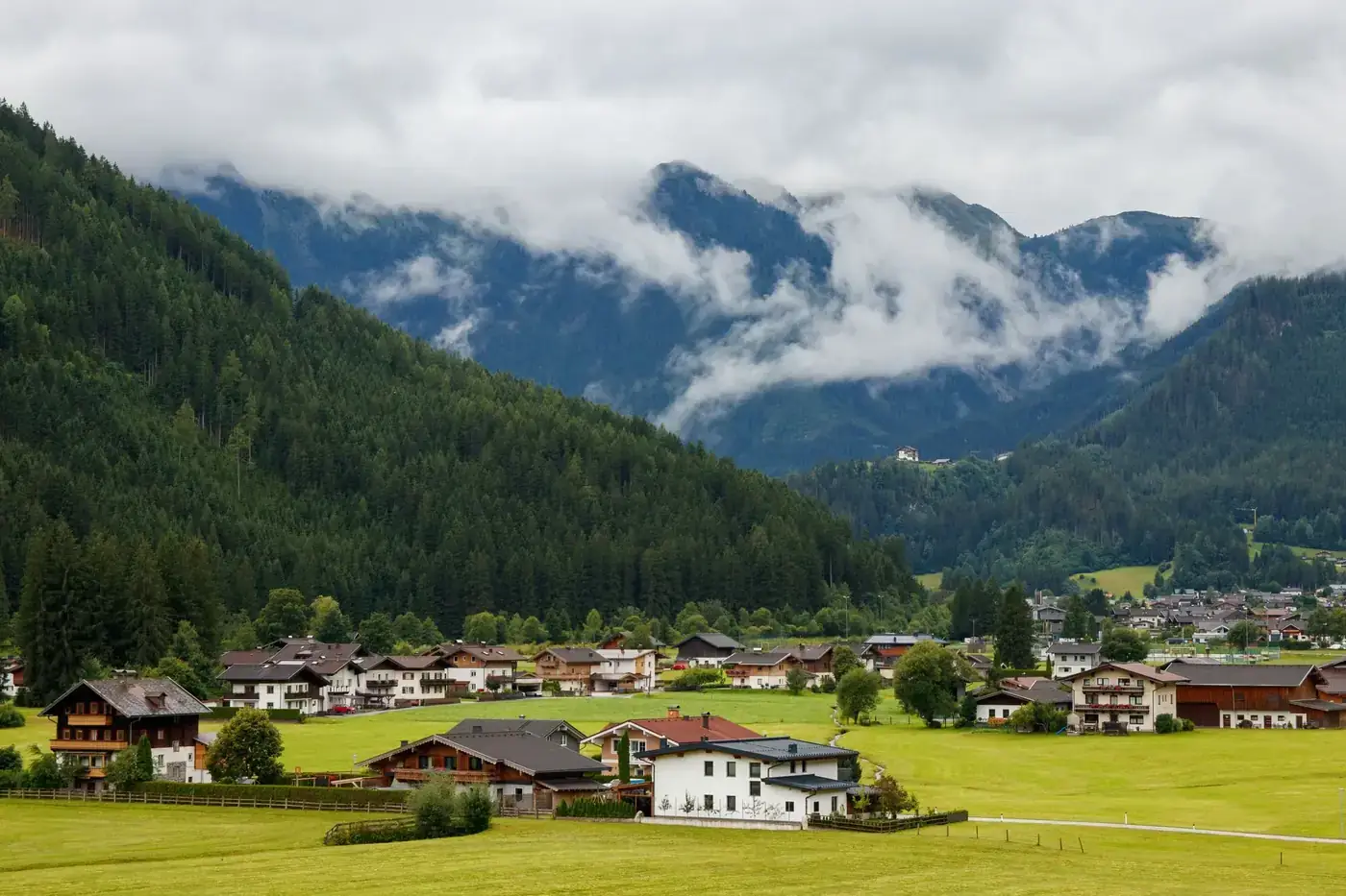 Charming alpine village nestled in lush, misty mountains on a cloudy day.