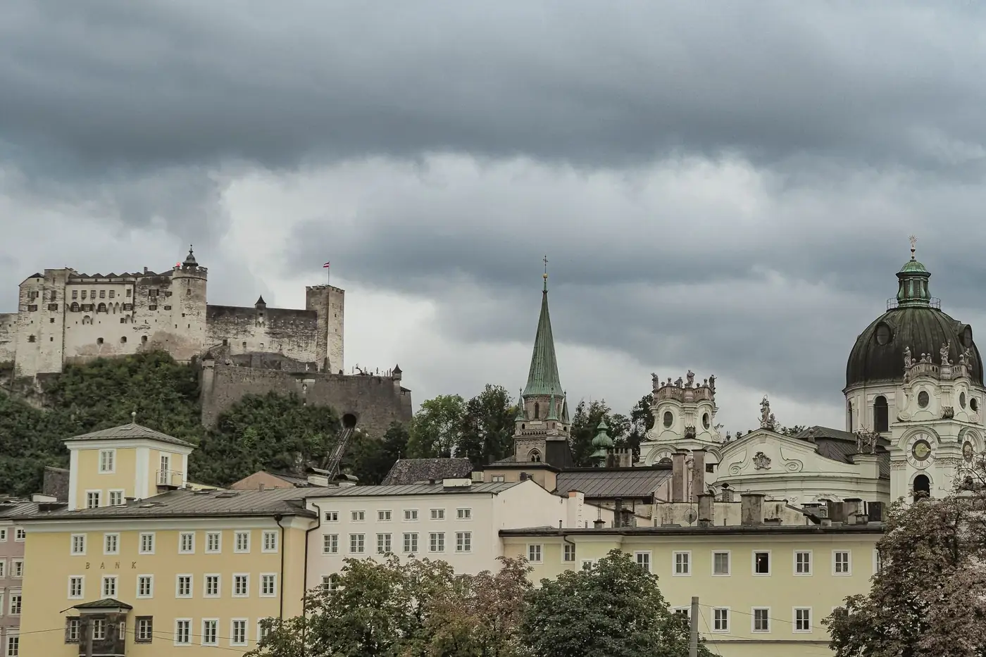 View of Salzburg's historic architecture with Hohensalzburg Fortress under cloudy skies.