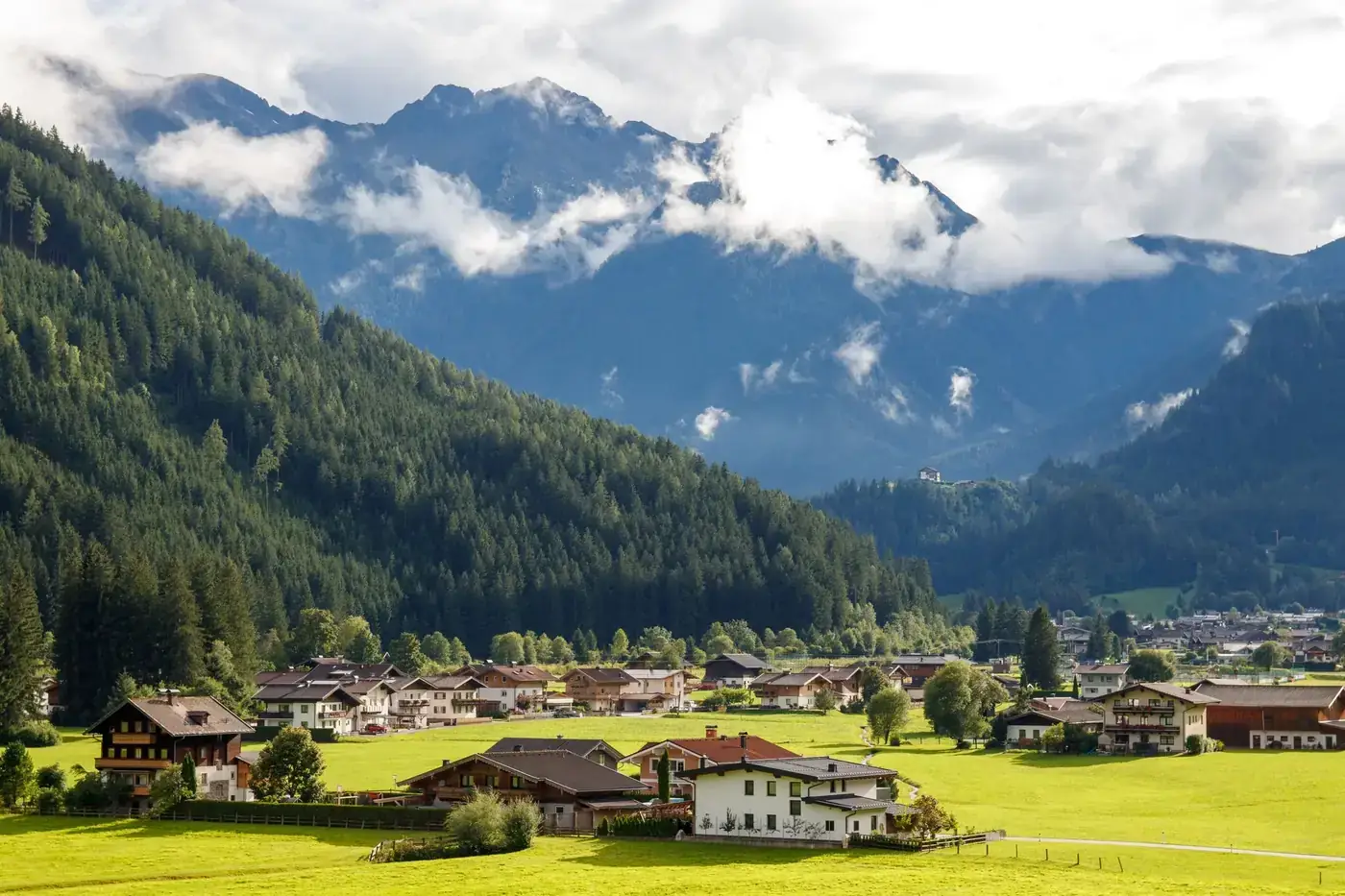 Charming Alpine village nestled against dramatic mountain backdrop under a cloudy sky.