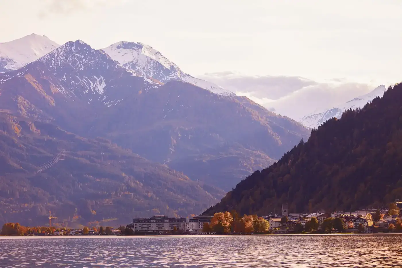 Picturesque view of a lakeside town against snow-capped mountains at sunset.